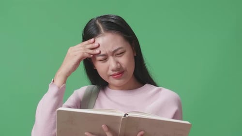 Asian Woman Student Reading A Book And Having Headache In Green Screen Studio