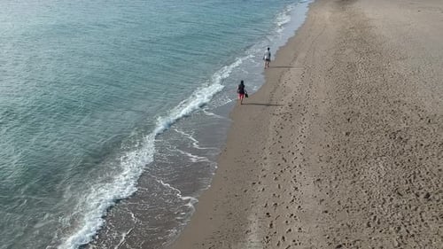 Vistas aéreas sobre una playa con olas suaves y gente caminando tranquilamente por la orilla.
