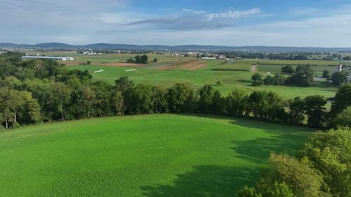 Green farmland in USA during summer months. Aerial rising shot revealing vast fields and farms in ru