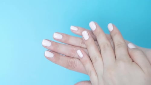 Female hand applies and rubs moisturizer on blue background, top view.