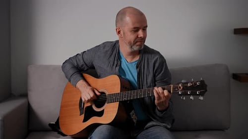 Man Plays Guitar Sitting on Couch At Home