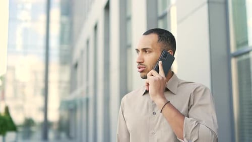 Close up. Young calm businessman talking on a smartphone while standing on the street near an office