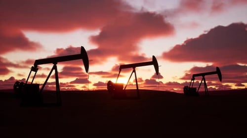 Oil Pumpjacks Silhouetted Against A Colorful Sunset In An Open Field