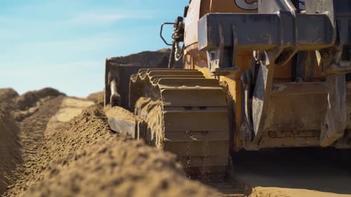 Bulldozer Machine Moves on Sandy Surface Leaving Tracks