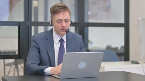 Mature Adult Businessman with Headset Talking Online with Customer in Call Center
