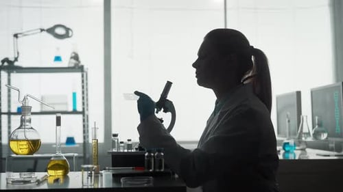 Side View of a Dark Silhouette of a Female Scientist Looking Under a Microscope Doing an Analysis of