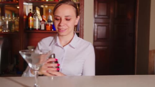 Female Bartender Shaking Shaker with Cocktail Pouring Alcoholic Drink Into Glass Standing Behind Bar