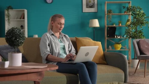 A Woman in Casual Clothes Sits on a Sofa in the Living Room with a Laptop on Her Lap A Woman Works