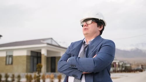 Audit manager in a protection helmet stands on a street in the suburbs with his arms crossed