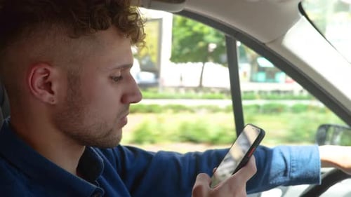 Young Handsome Serious Man Driving a Car and Typing on Smartphone While Looking at Road