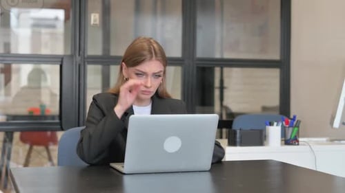 Young Woman Rubbing Temples in Office with Laptop