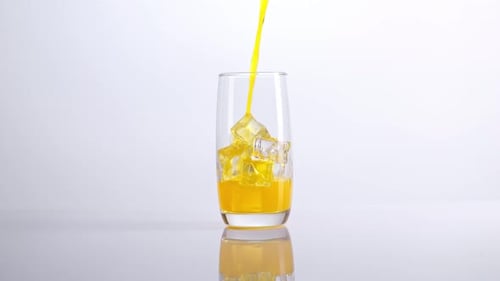 Yellow Drink Poured into Glass with Ice Cubes