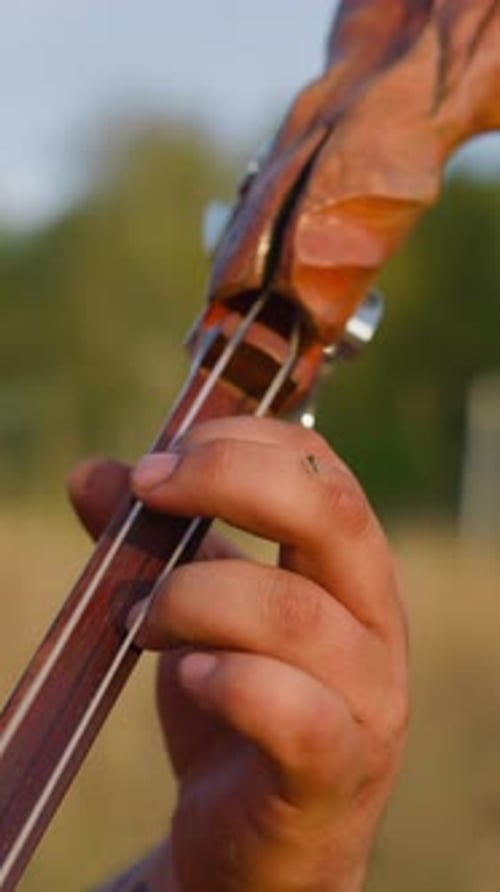 Músico folclórico presiona cuerdas en cubierta tocando Ikili en el campo