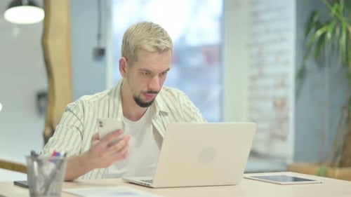 Man Uses Mobile and Laptop at Office Desk