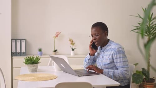 Businesswoman multitasking while working at her home office desk using a laptop and smartphone