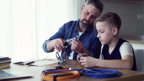 Mature Father with Small Son Sitting at Table Indoors, Working on School