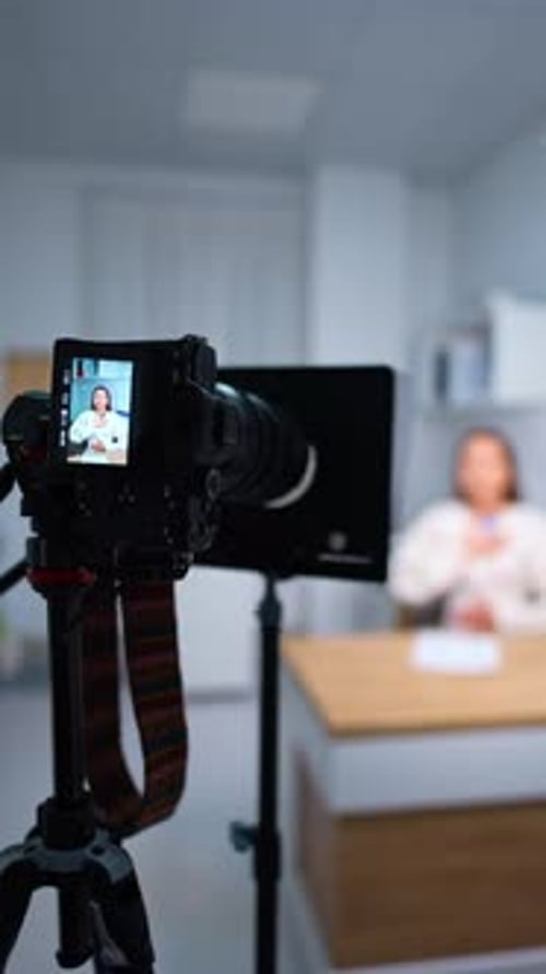 Professionelle Kamera auf einem Stativ, die einen Sprecher am Schreibtisch fotografiert. Blogging-Konzept. Verschwommener
Hintergrund