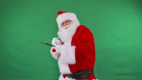 Santa Focuses on His Tablet Against a Green Screen Ideal for Holiday Planning