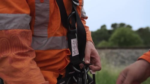 Gros plan d'un cheminot vêtu de vêtements orange à haute visibilité attachant un harnais de sécurité avec