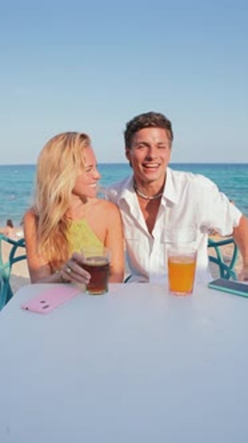 Vertical Joyful Couple Enjoying Refreshing Drinks at a Sunny Beach Terrace with Stunning Ocean Views