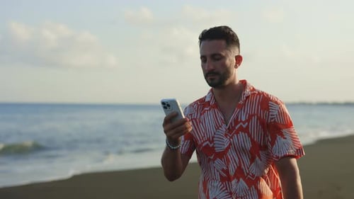 Young Handsome Multiethnic Guy Walking on Beach and Text Messaging Using Smartphone Man in the