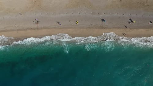 People Sunbathing at Deserted Beach with Scenic Turquoise Waves Crushing on the Coast
