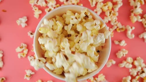 Popcorn grains falling into red and white striped bucket isolated on pink background