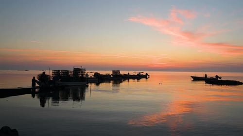 Silhouettenfischer, der Fischfallen auf Holzbooten auf dem Wasser zum Pier zieht und sich farbenfroh spiegelt