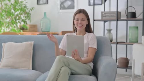 Young Woman Doing Video Chat on Tablet while Sitting on Sofa at Home