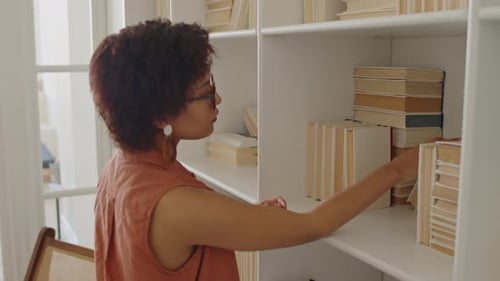 Black Woman Choosing Book to Read from Home Library