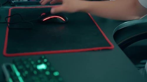 RGB-Gaming-Maus mit der Hand des Spielers auf einem Mauspad, Computerspielvorgang in Nahaufnahme,