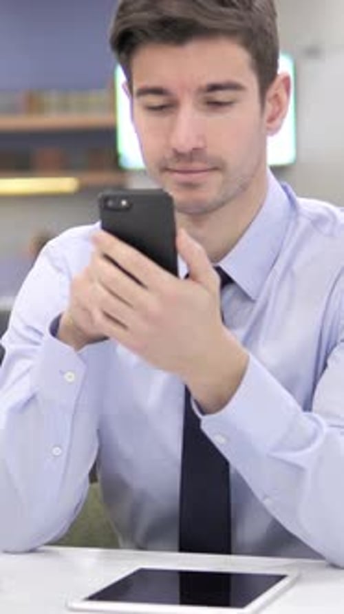 Young Man Uses Smartphone in Office Setting