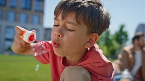 Young Boy Blowing Bubbles in Park on Sunny Day