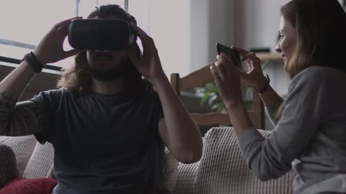 Woman Records Man Experiencing Virtual Reality Headset at Home