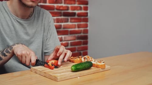 Young Adult Cuts Tomato for Bread Topping