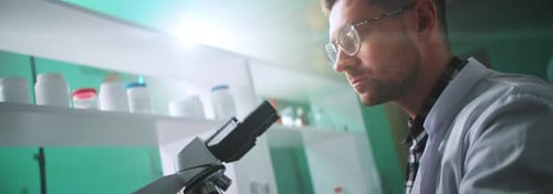 Young Adult Man Examines Specimen with Microscope