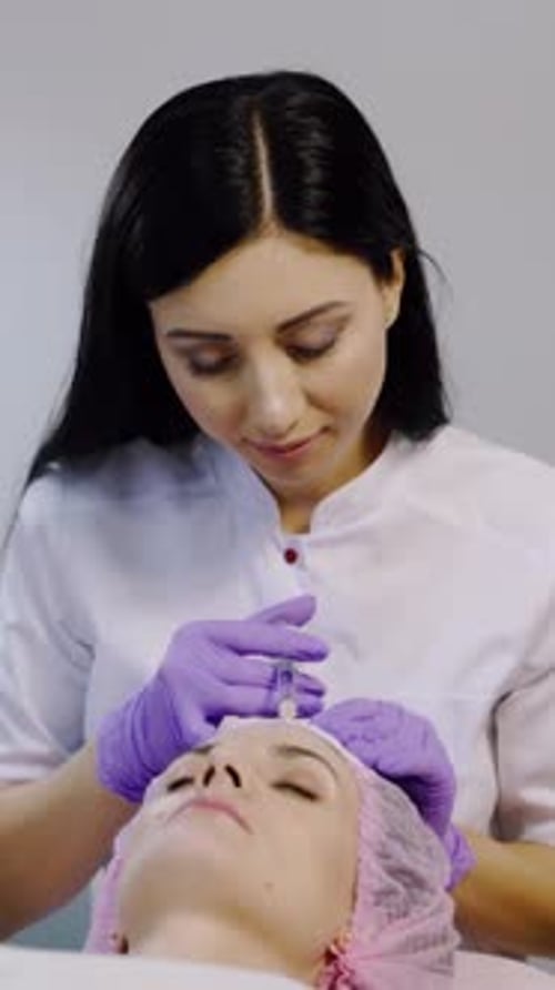 A woman on the procedure of injections in a cosmetology clinic. Preventing wrinkles. Vertical video