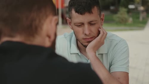 Man Listens Thoughtfully to Friend Outside in Park