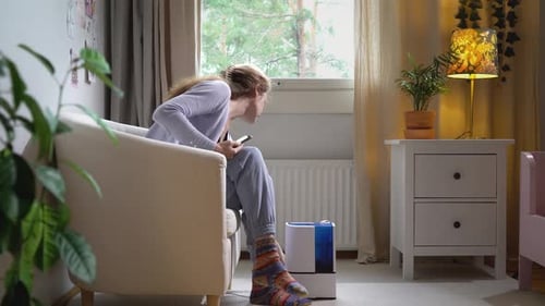 Eine hübsche junge Frau schaltet einen modernen Luftbefeuchter im Wohnzimmer ein
