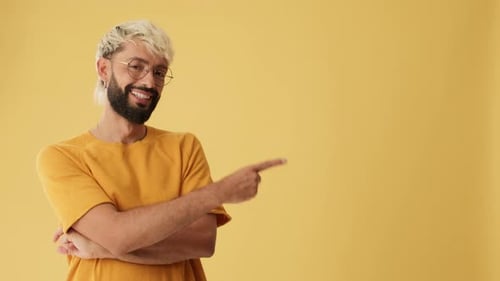 Smiling man pointing fingers to show mockup space, isolated on yellow background in studio