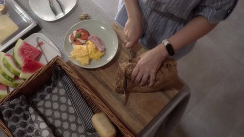 Woman cuts bread for breakfast. There are eggs, ham and mozzarella on the plate.