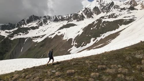 Man Hiking Across Grassy Hill in Mountains