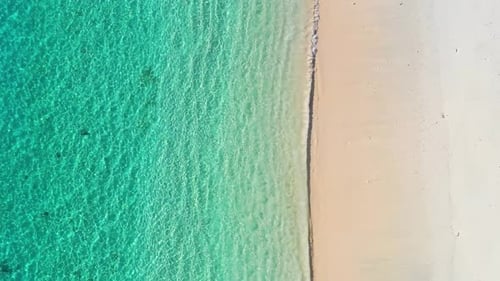 Aerial drone view of calm turquoise waves and a sandy tropical beach.