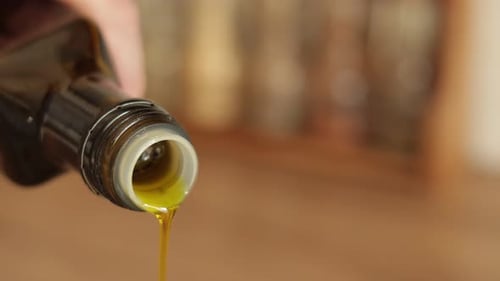 Pouring olive oil from glass bottle. Bottle Neck of Olive Oil Pouring Down a Macro Shot