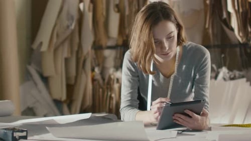 Der Bekleidungsdesigner benutzt ein Tablet, während er sich an einen Studiotisch lehnt.