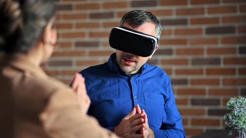 Mann benutzt ein Virtual-Reality-Headset in einem Büro, während Frau erklärt und gestikuliert