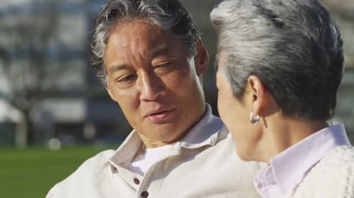 Happy Senior Couple Sitting on Park Bench Together 50-55