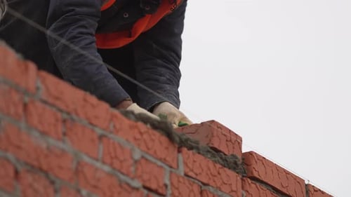 Worker in Gloves and Helmet Places New Brick Into Row