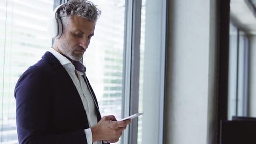 Mature businessman with smartphone listens to music in sunny office