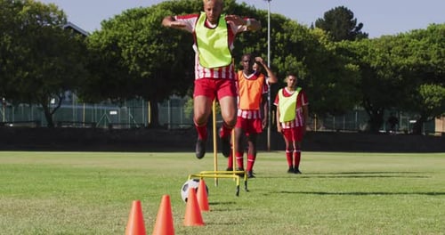 Video of diverse group of male football players warming up on field, running and kicking ball